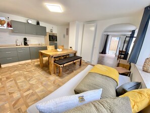 A modern interior with a wooden dining table, grey cabinets, a sofa with cushions, and a visible kitchen area. - Apartment 'Ferienwohnung Kleinôd' with Private Terrace and Wi-Fi (Bendorf)