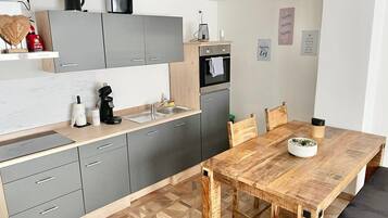 Een moderne keuken met grijze kastjes, een houten eettafel en een koffieapparaat.