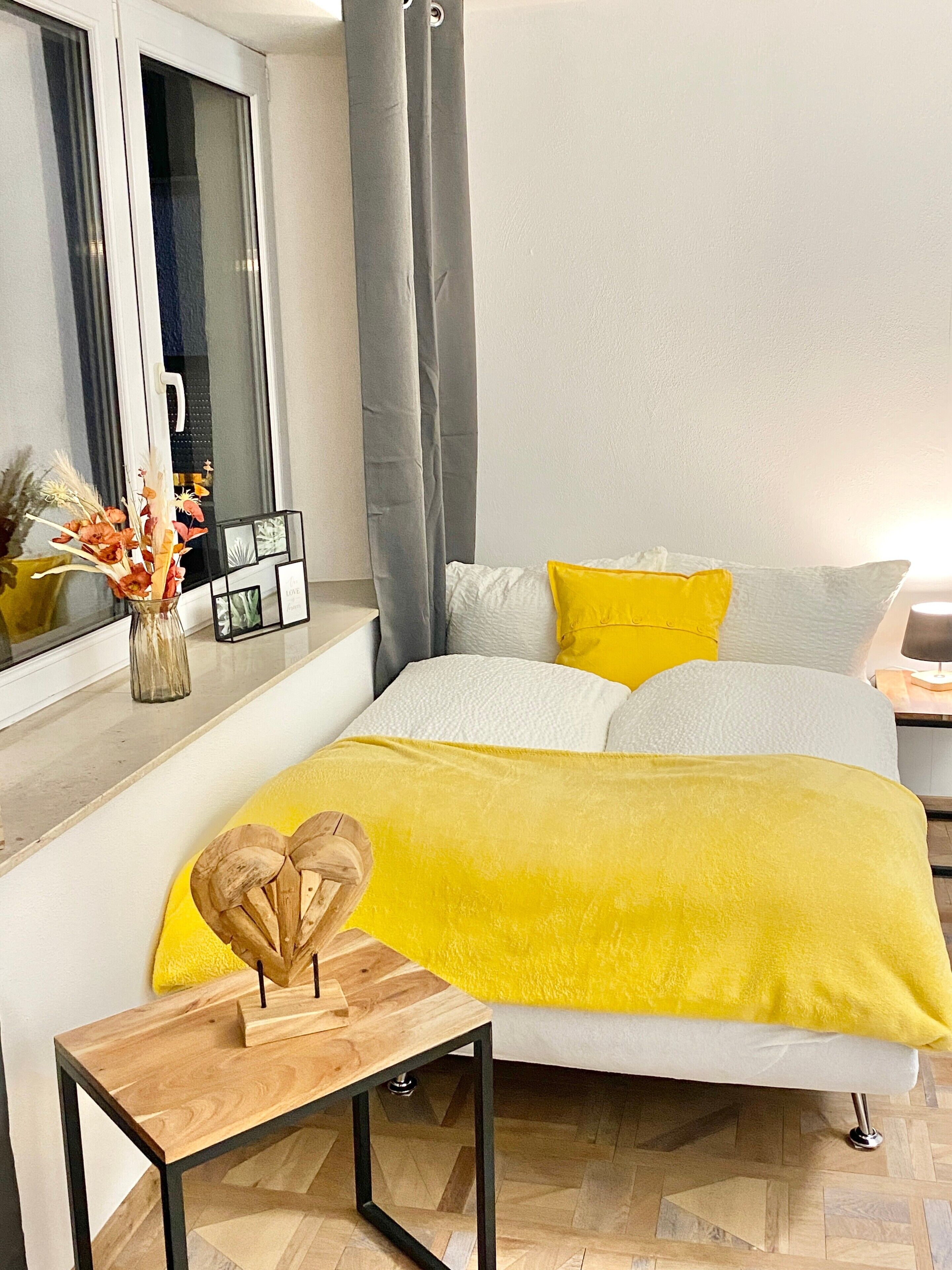 Ein modernes Schlafzimmer mit Bett, Nachttisch, Spiegel und einem Fenster mit Vorhängen.