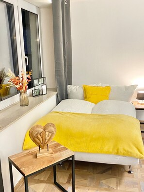 Ein modernes Schlafzimmer mit Bett, Nachttisch, Spiegel und einem Fenster mit Vorhängen.