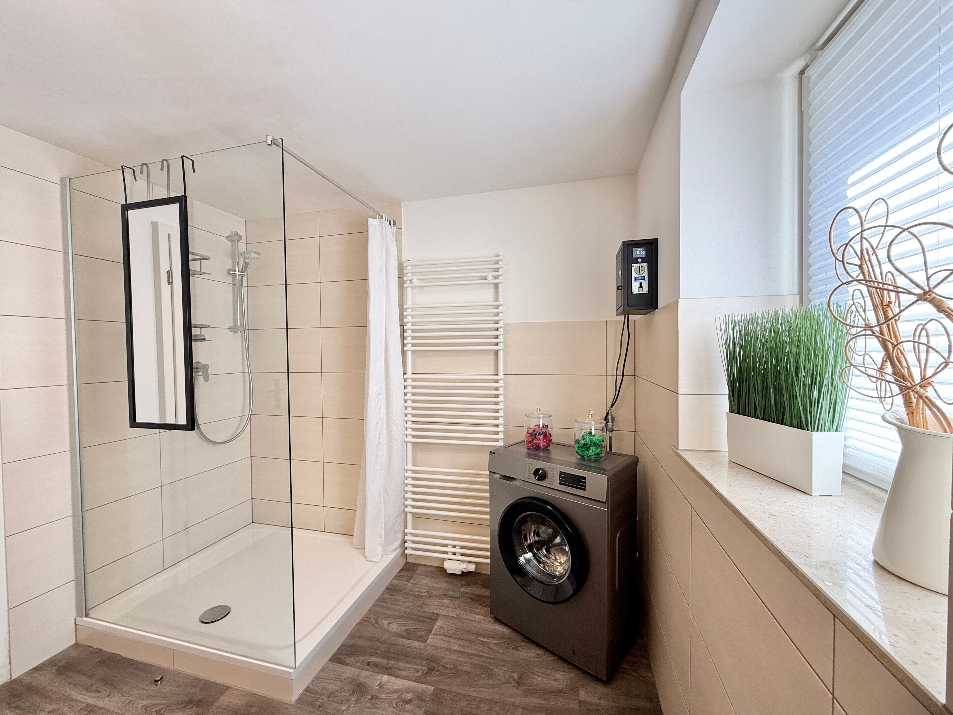 A modern bathroom with a glass shower enclosure, a built-in washing machine, and a radiator.