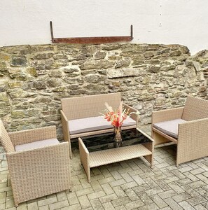 Eine Steinsäule mit einem Gartenmöbel-Set aus Weidengeflecht, bestehend aus zwei Stühlen und einem Tisch.