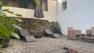 Een terras buiten, met een stenen muur, een zithoek met lounge fauteuils en een potplant.