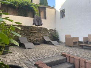 An outdoor patio with a stone wall, a seating area with lounge chairs, and a potted plant.