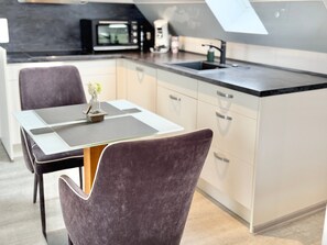 A modern kitchen with a central island, a dining table with chairs, and a microwave in the background. - Apartment 'Rose' with Mountain View, Wi-Fi and Air Conditioning (Höhr-Grenzhausen)