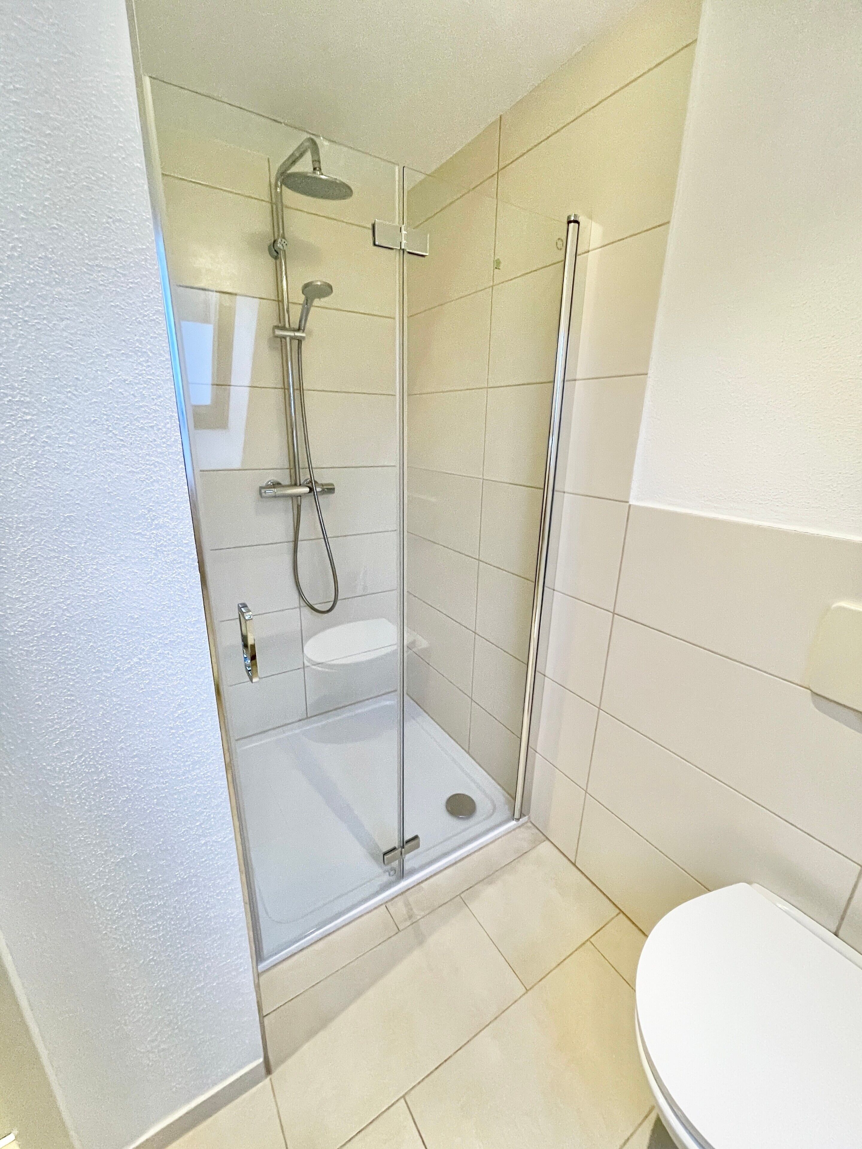 Ein Badezimmer mit einer Duschkabine aus Glas, einer Toilette und Fliesenwänden.