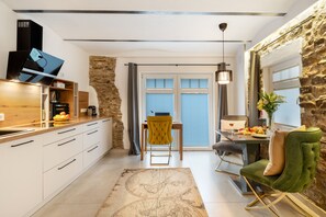 Une cuisine moderne avec un mur d’accent en pierre, un coin repas avec une table dressée pour deux personnes, et une vue à travers la porte vitrée.