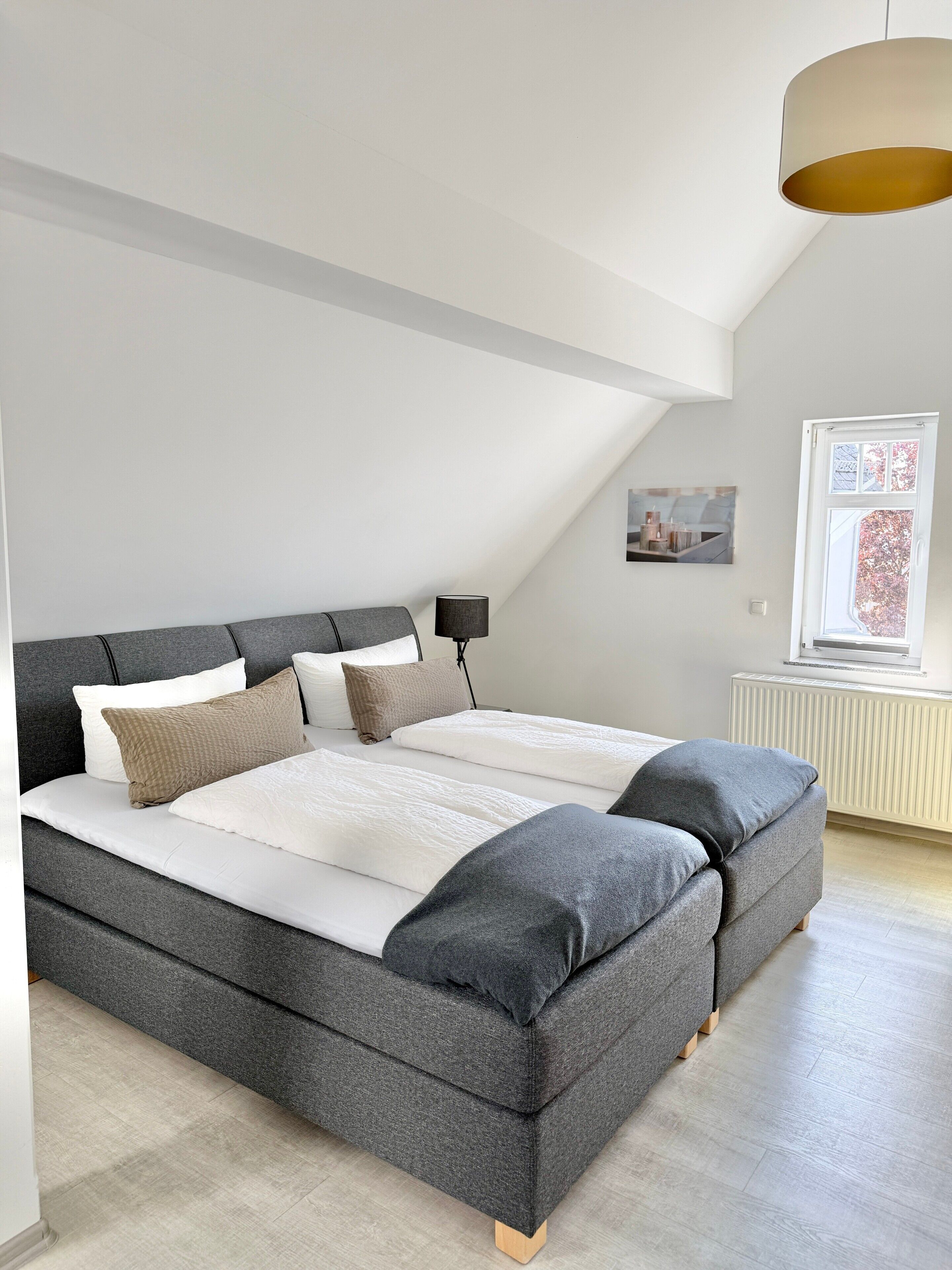 A modern bedroom with a large bed, a side table, and a window with a view.