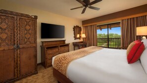 Een hotelkamer met een groot bed, een flatscreen televisie, een plafondventilator, een balkon met gordijnen en een houten garderobekast.