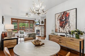 A modern living room with a fireplace, a round dining table, and a large abstract painting. - Luxury Mountain Escape | Steps to Snowflake Lift with Resort Amenities (Breckenridge)