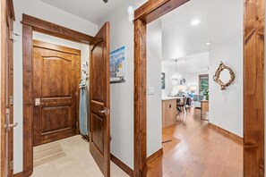 A hallway with wooden doors, a kitchen area with a dining table, chairs, and a chandelier. - Luxury Mountain Escape | Steps to Snowflake Lift with Resort Amenities (Breckenridge)