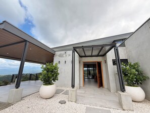 A modern building with a covered entrance, large potted plants, and a view of the landscape. - Cloud Forest Villa (Valle Azul)