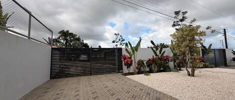 A paved outdoor area with a fence, a gate, and various plants.