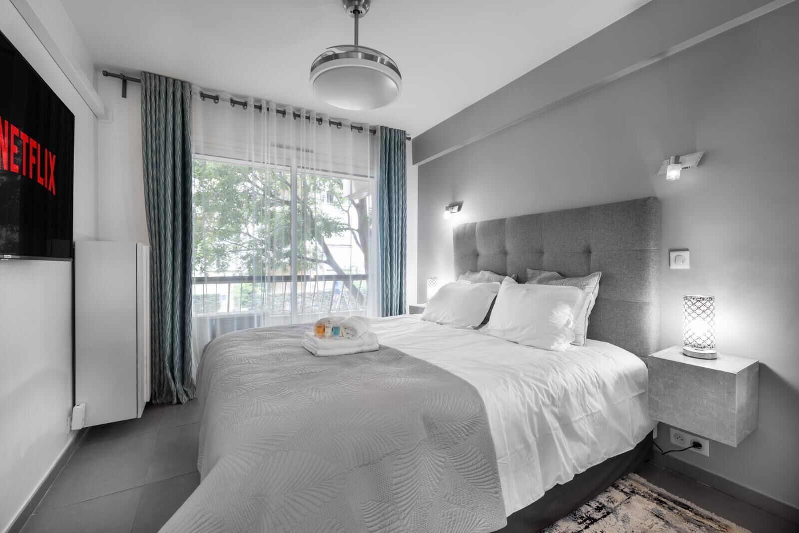 A modern hotel room with a large bed, a flat-screen TV, and a view of the outdoors.