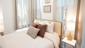 Ein ordentlich bezogenes Bett mit Kopfteil, ein Nachttisch mit Lampe und ein an der Wand hängendes Bild.