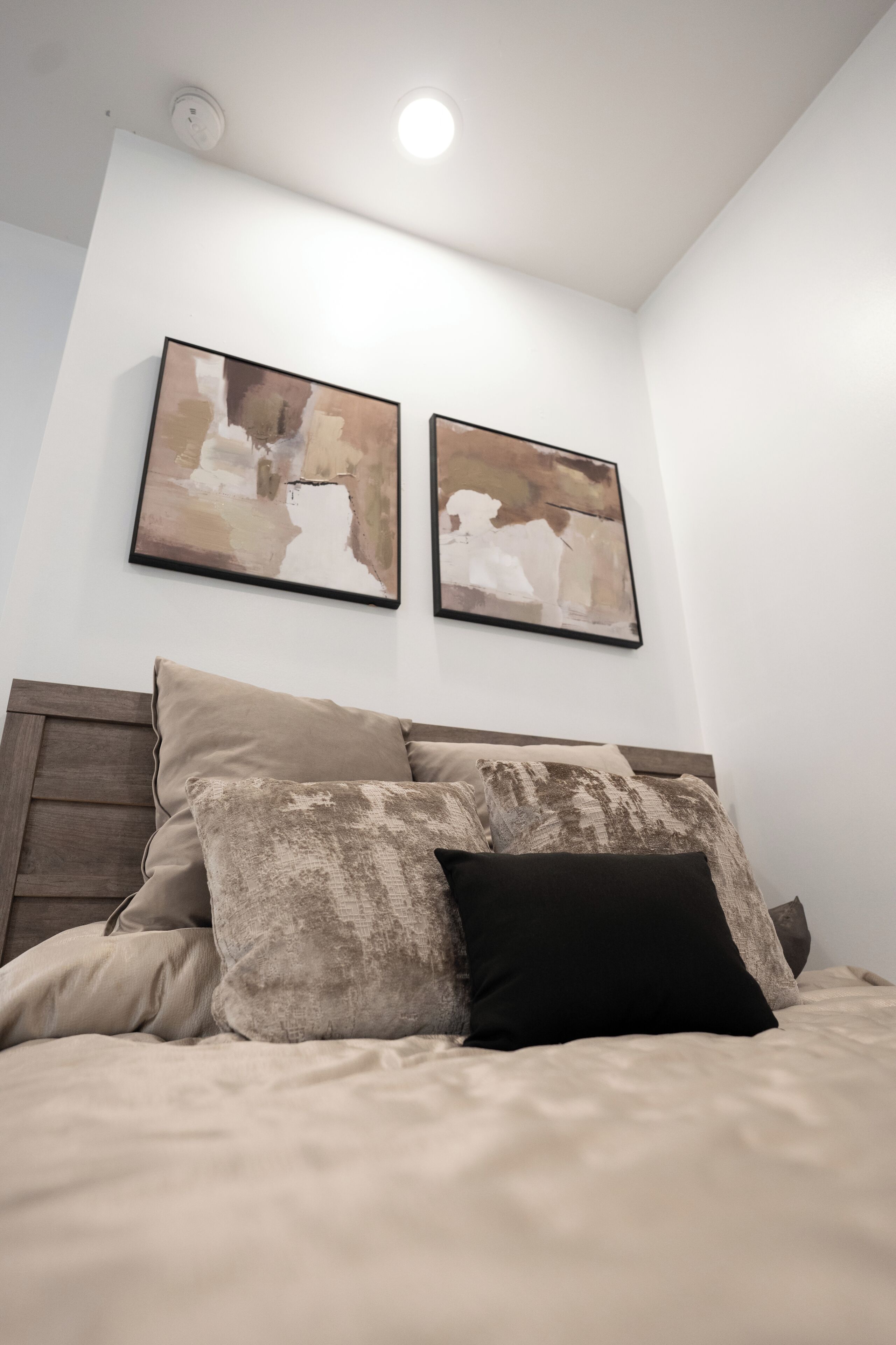 Un dormitorio con una cama, almohadas y dos cuadros abstractos en la pared.