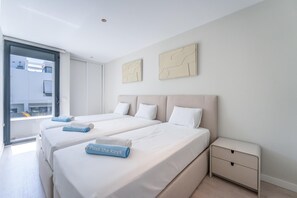 Quarto de hotel com duas camas, uma mesinha de cabeceira e uma janela com vista para prédios.