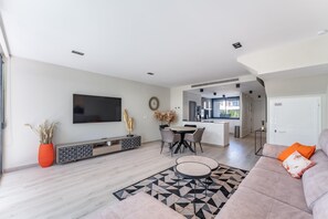 A modern living room with a flat-screen TV, a dining area, and a kitchen in the background. - 3 Bed Townhouse Escape Costa Del Sol - Pass the Keys (Fuengirola)