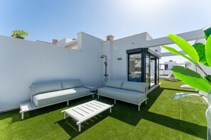 Un espace de vie extérieur moderne comprenant un canapé, une petite table et une structure vitrée.