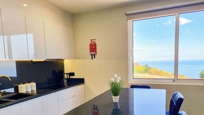 Een moderne keuken met een zwart aanrecht, witte kasten en een raam met uitzicht op zee.