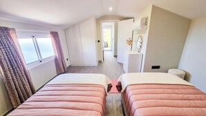 Een hotelkamer met twee bedden, een kledingkast, een kaptafel en uitzicht op de gang.