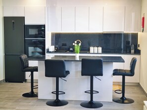 A modern kitchen with a central island, bar stools, a black refrigerator, and a microwave. - Betty's House, Ocean and Hillside View (Fajã da Ovelha)
