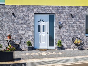 A building facade with a stone-textured wall, a white door, and a small outdoor seating area with a table and chairs. - Betty's House, Ocean and Hillside View (Fajã da Ovelha)
