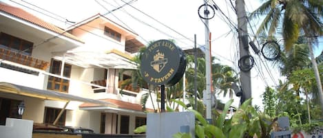 A hotel sign with a circular emblem, a multi-story building with balconies, and a tropical environment with palm trees.