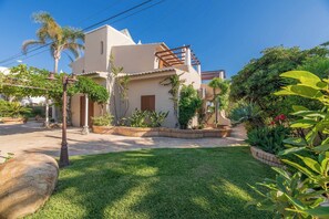 Una casa de dos pisos amb un pati, envoltada de vegetació exuberant i un jardí ben cuidat.