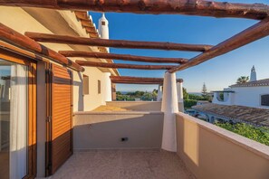 Un balcó amb una pèrgola de fusta, una porta corredissa de vidre i vista al mar i als edificis.