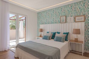 A bedroom with a bed, pillows, bedside tables, a window with curtains, and a patterned wall. - Casa da Praia - Four Bedroom Villa, Sleeps 8 (Algarve)