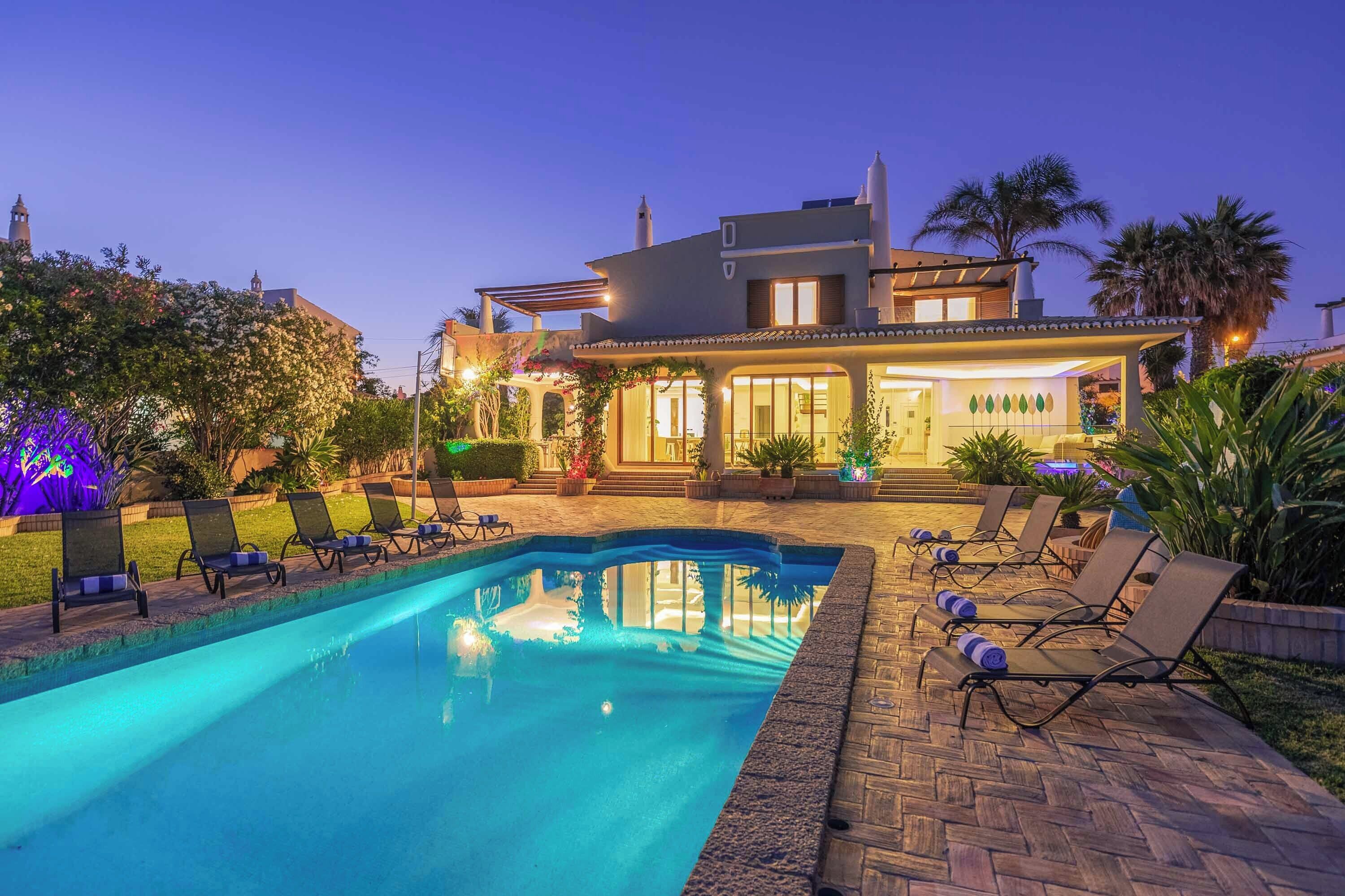 A two-story house with a swimming pool, lounge chairs, and a garden.
