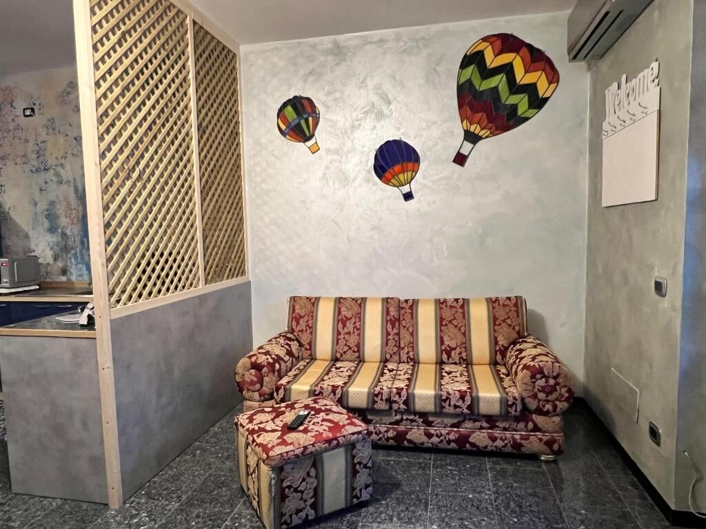Une pièce comprenant un canapé et un pouf, une cloison en bois et un mur orné d’une pancarte « Bienvenue ».