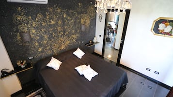 A hotel room with a bed, a chandelier, a mirror, and a decorative wall.