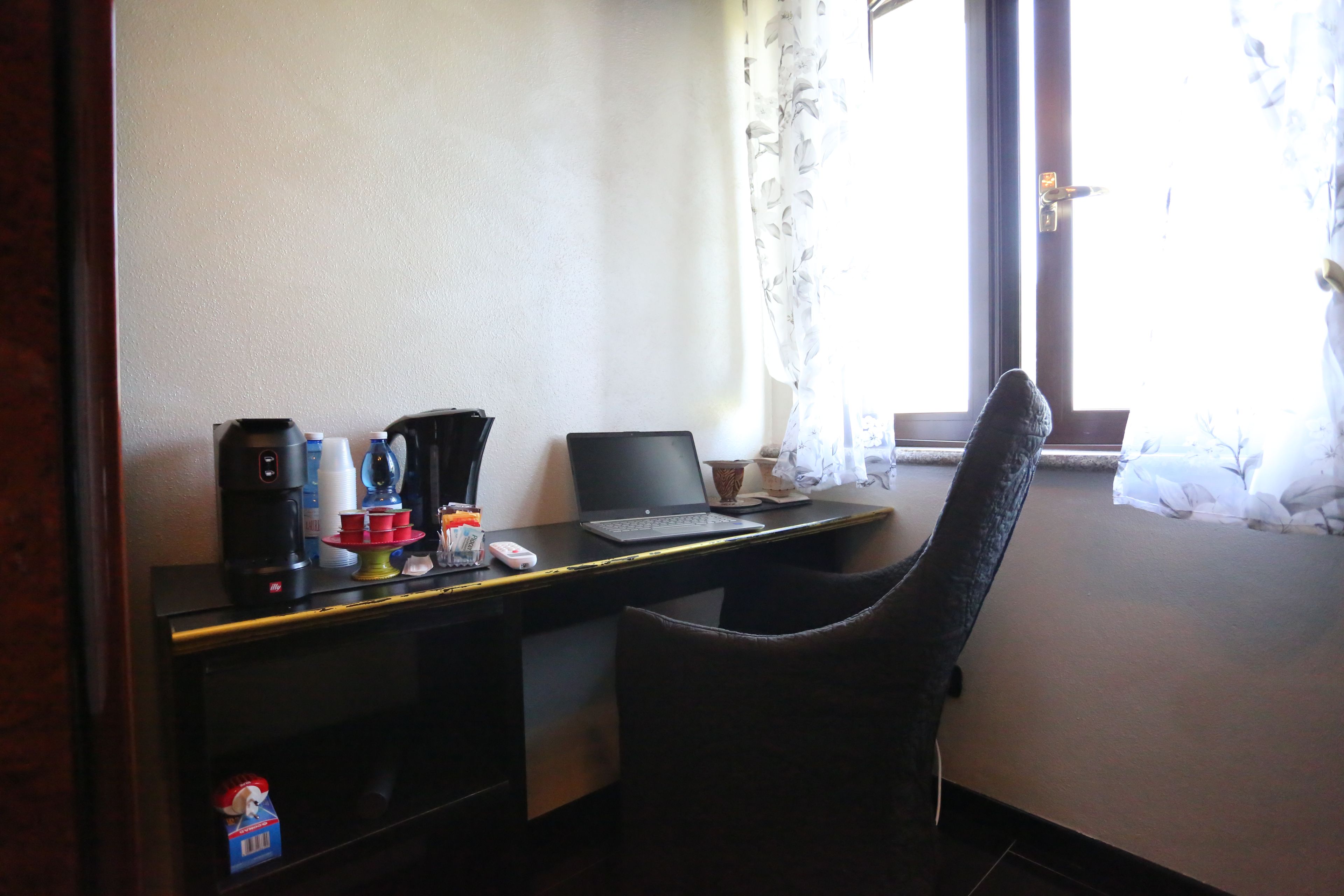 Una camera d'albergo con una scrivania, un portatile, una macchina per il caffè e una sedia.