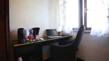 Una camera d'albergo con una scrivania, un portatile, una macchina per il caffè e una sedia.
