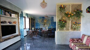 A spacious living area with a large flat-screen TV, a chandelier, a dining table with chairs, and a sofa.