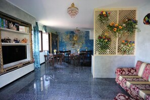 A spacious living area with a large flat-screen TV, a chandelier, a dining table with chairs, and a sofa.
