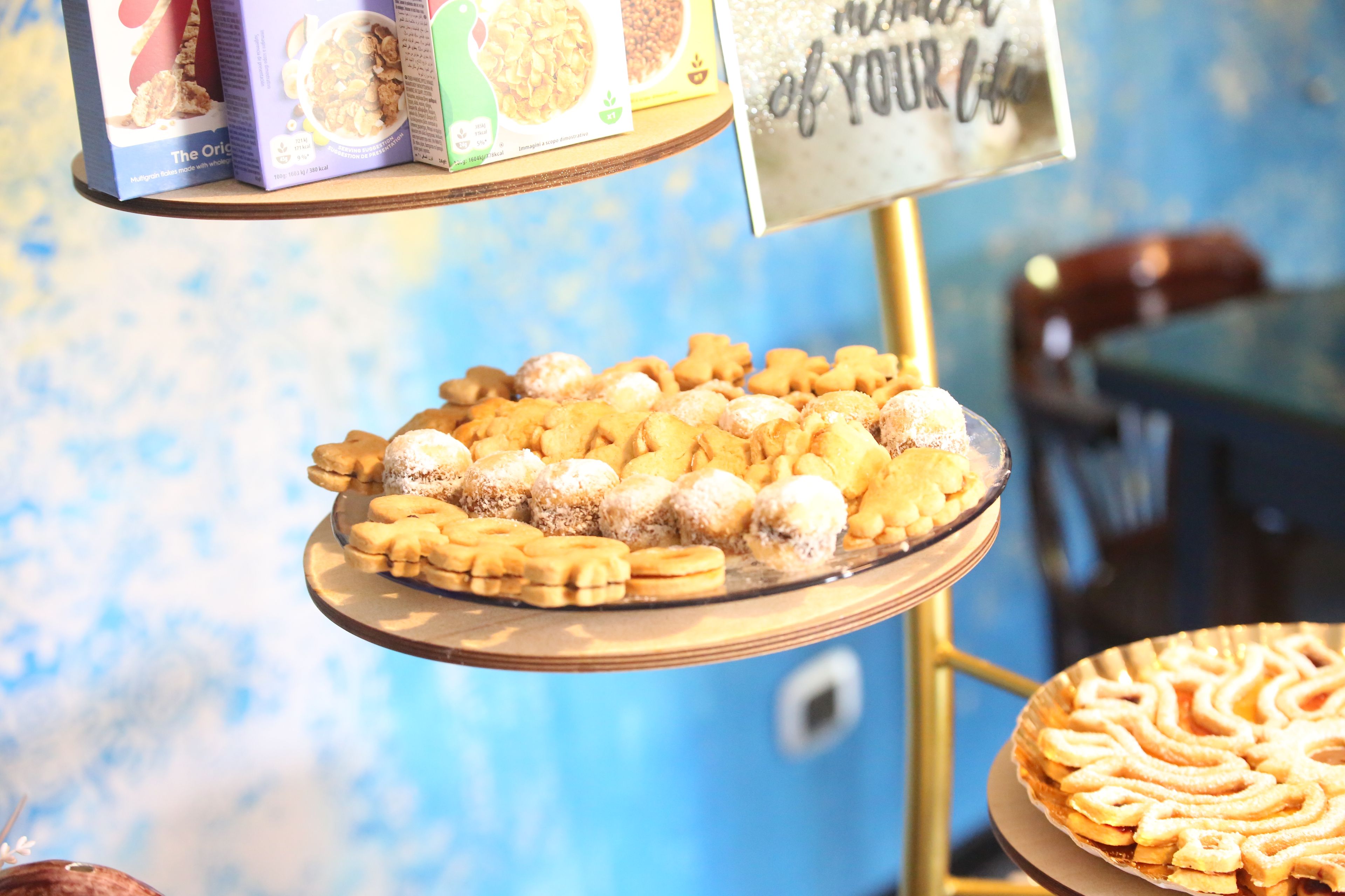 Une variété de pâtisseries est présentée sur un présentoir en verre, avec une pancarte placée au-dessus.