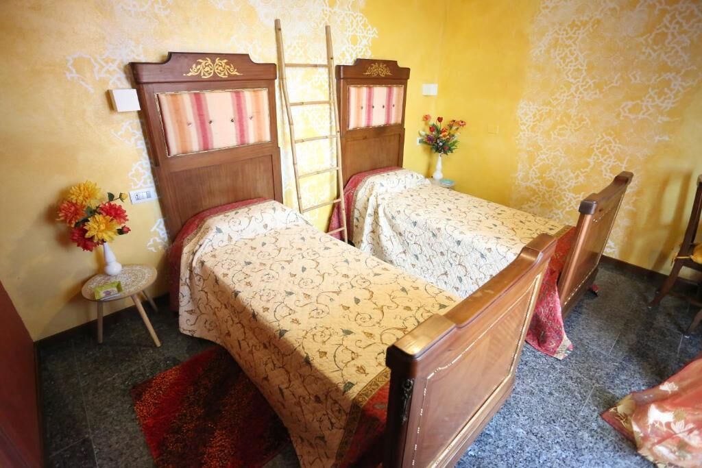 A room with two beds, a small table with a vase of flowers, and a ladder leaning against the wall.