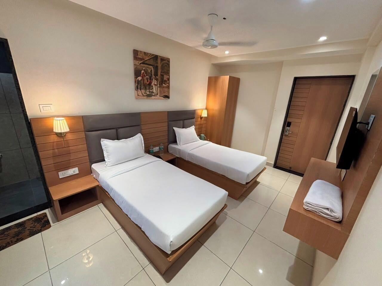 Habitación de hotel con dos camas, televisión, un cuadro en la pared y un mueble de madera.
