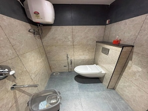 A small, tiled bathroom with a toilet, a hand dryer, a soap dispenser, and a trash bin.