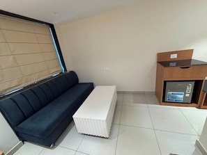 A room with a dark blue sofa, a white rectangular table, and a small refrigerator.