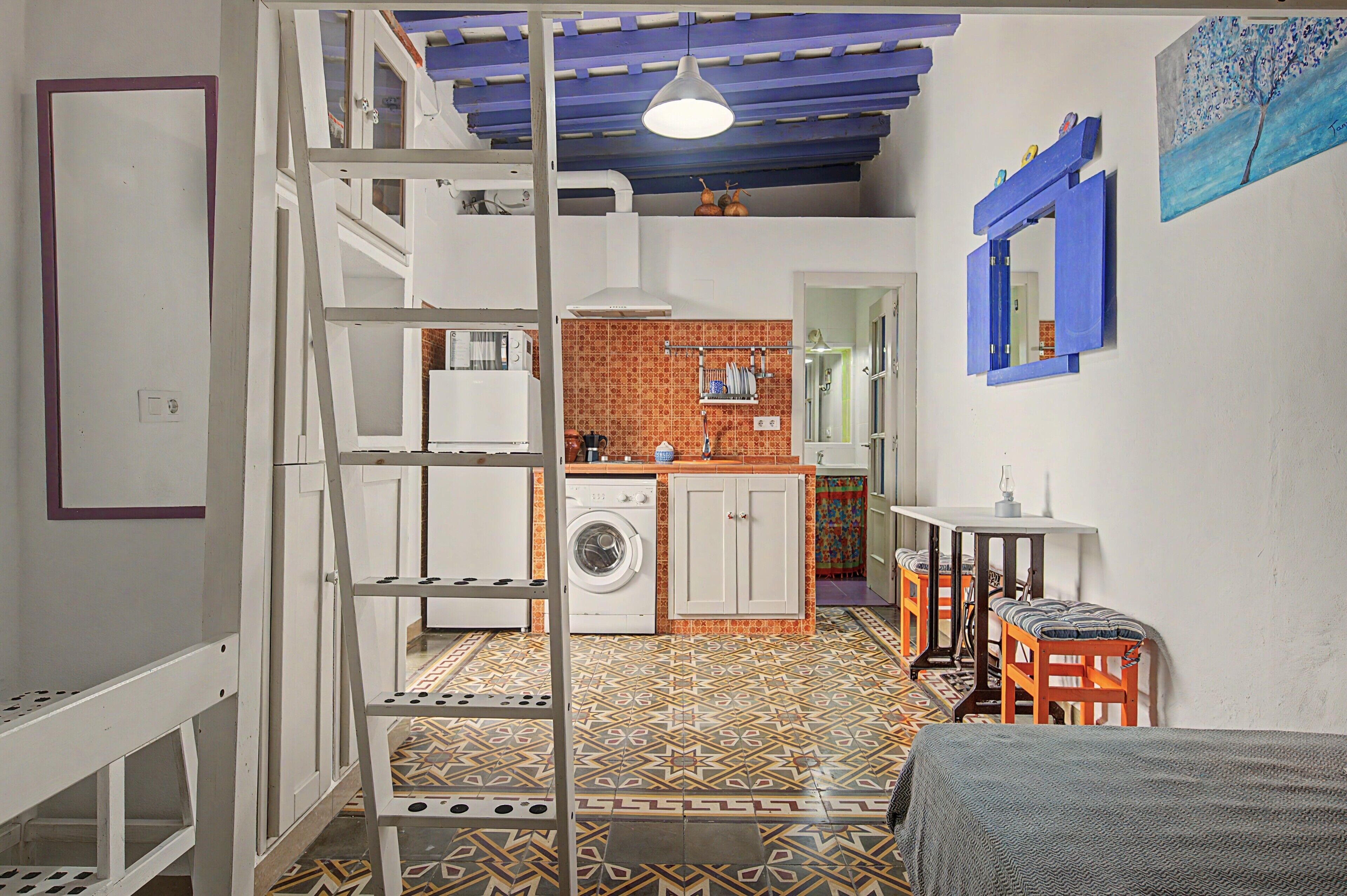 A compact kitchen with a washing machine, a dining area with a table and chairs, and a patterned floor.