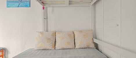 A bedroom with a bed, pillows, a painting, and a ceiling with colorful beams.