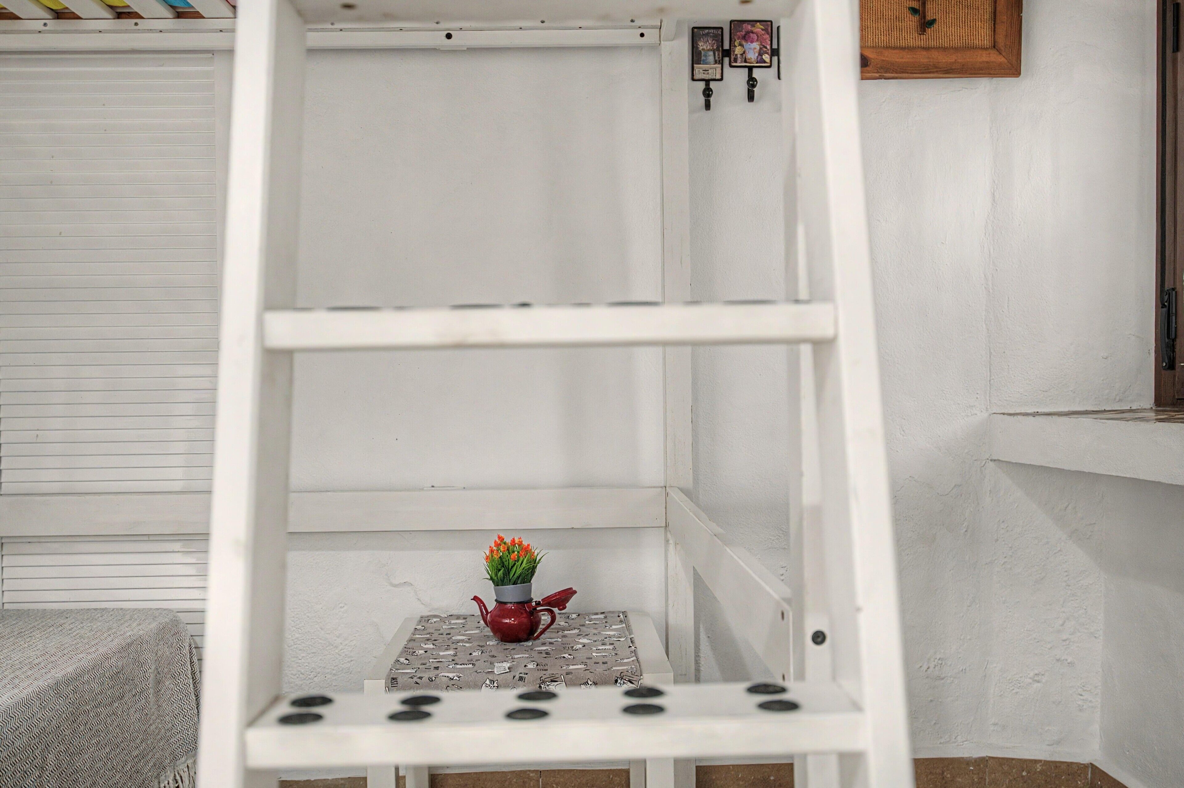 Une étagère en métal blanc, sur laquelle se trouvent une petite table et une théière rouge.