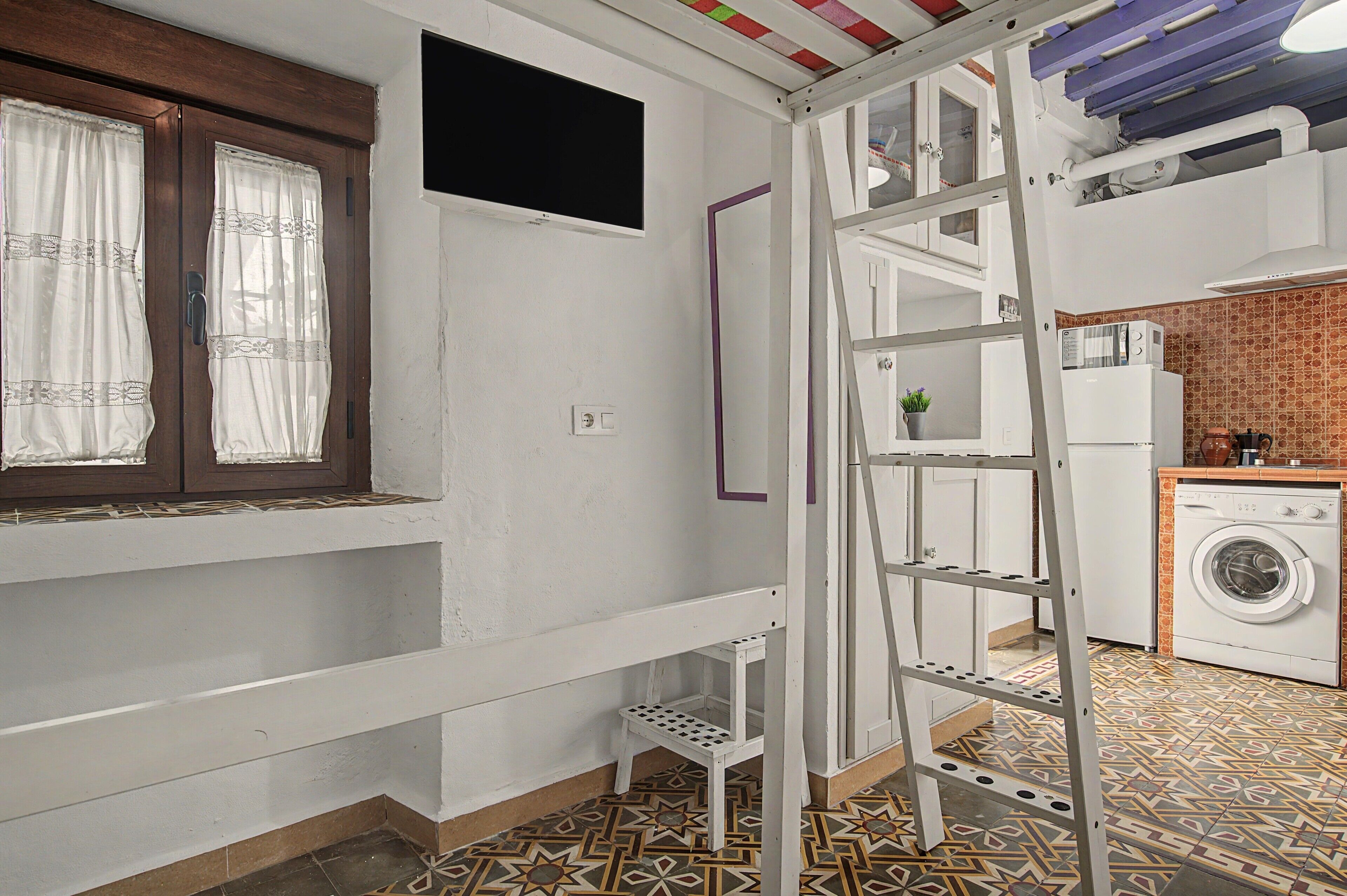 Una cocina pequeña con lavadora, una escalera y una ventana con cortinas.