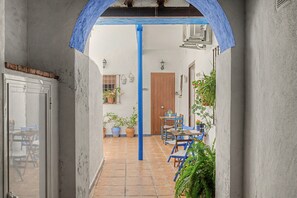A narrow corridor with a tiled floor leading to a room with a wooden door, a table with chairs, and potted plants. - Historic Center Studio – Terrace and Beach Nearby (Conil de la Frontera)