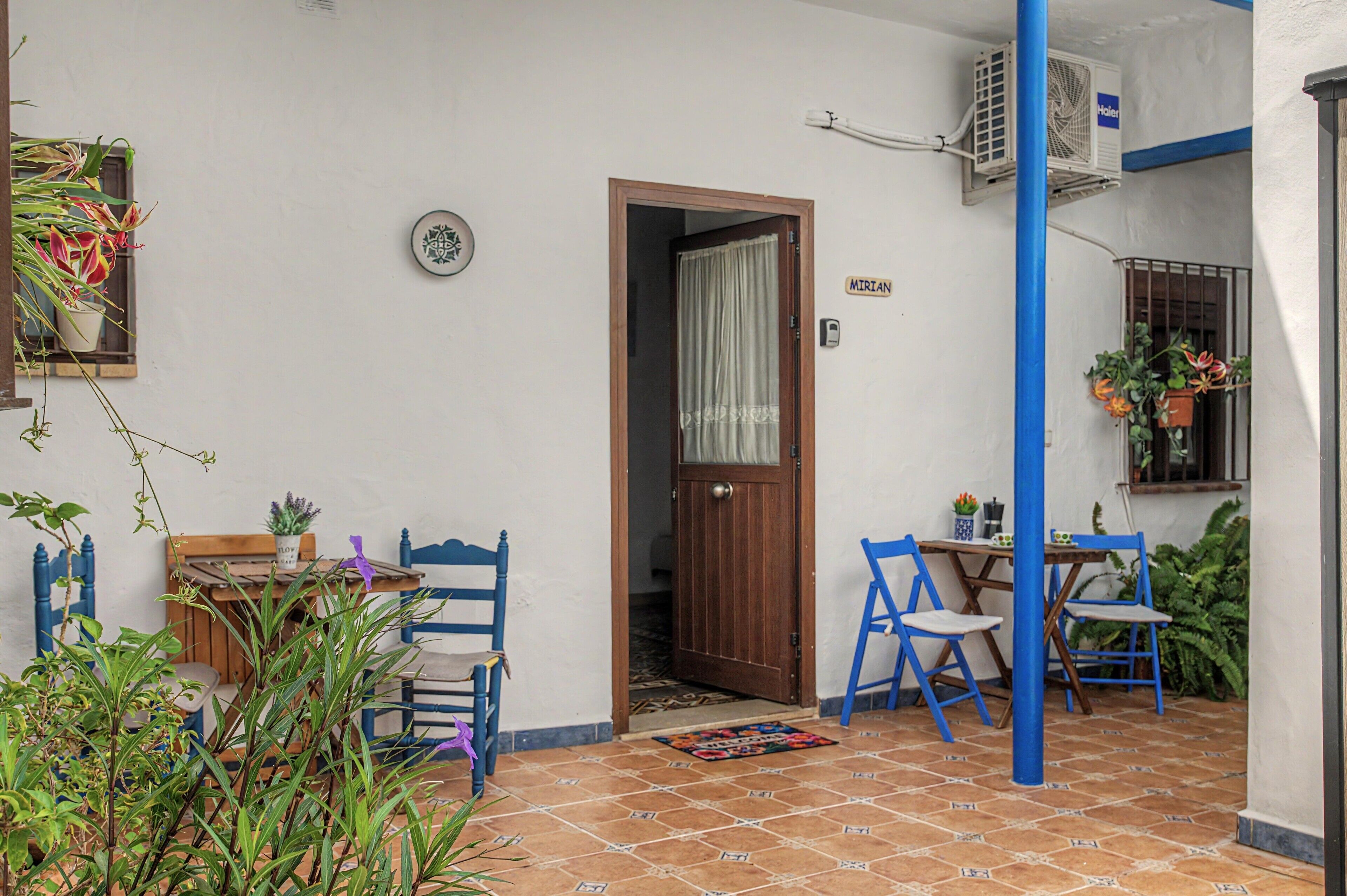 Un petit espace patio avec une table et des chaises en bois, une porte et un pilier bleu.
