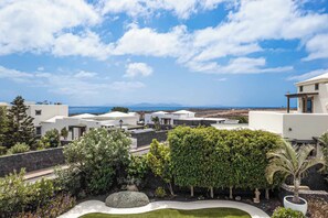 A residential area with modern white buildings, a landscaped garden with various plants, and a view of the sea. - Villa Aguamarina - Three Bedroom Villa, Sleeps 6 (Playa Blanca)
